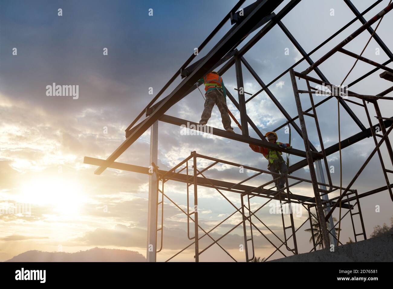 Silhouette d'ouvrier de construction sur la structure de toit dans le chantier de construction, concept équipement de hauteur de sécurité. Banque D'Images