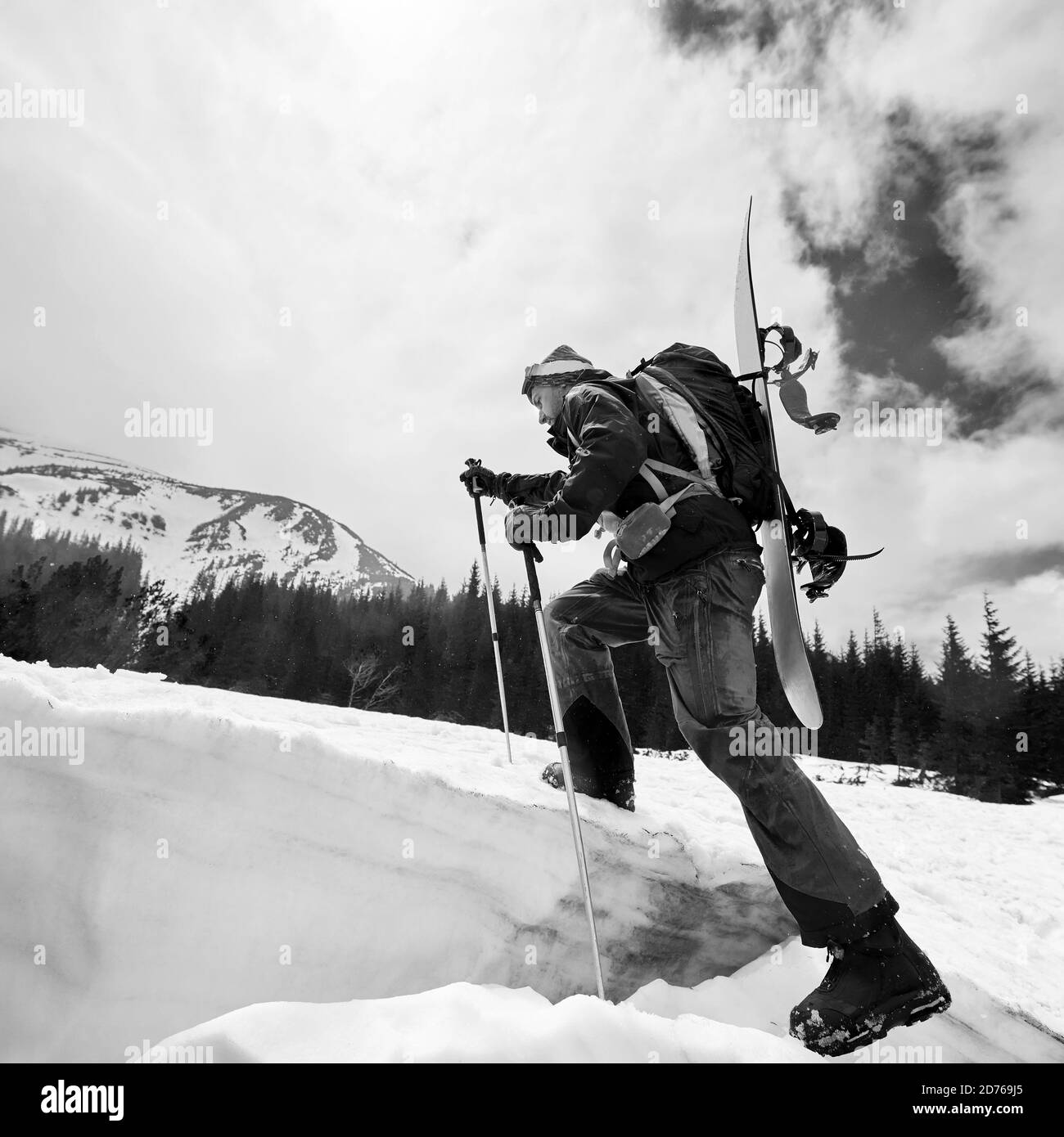 Mountaineer pendant le ski de fond marchant le long de la crête enneigée avec le snowboard et le sac à dos sur son dos. Vue à angle bas. Nuages blancs dans le ciel, neige- Banque D'Images