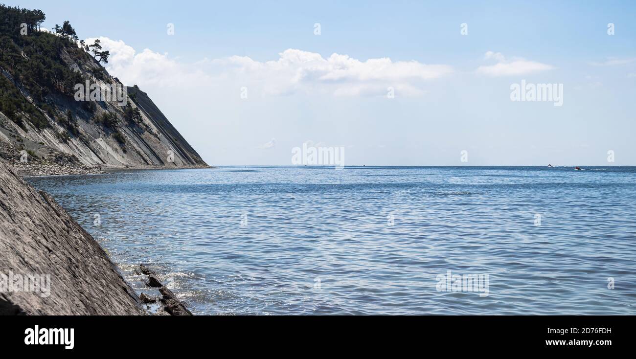 Panorama du paysage marin. Une plage sauvage en pierre pittoresque au pied des falaises et un ciel bleu vif avec des nuages Banque D'Images