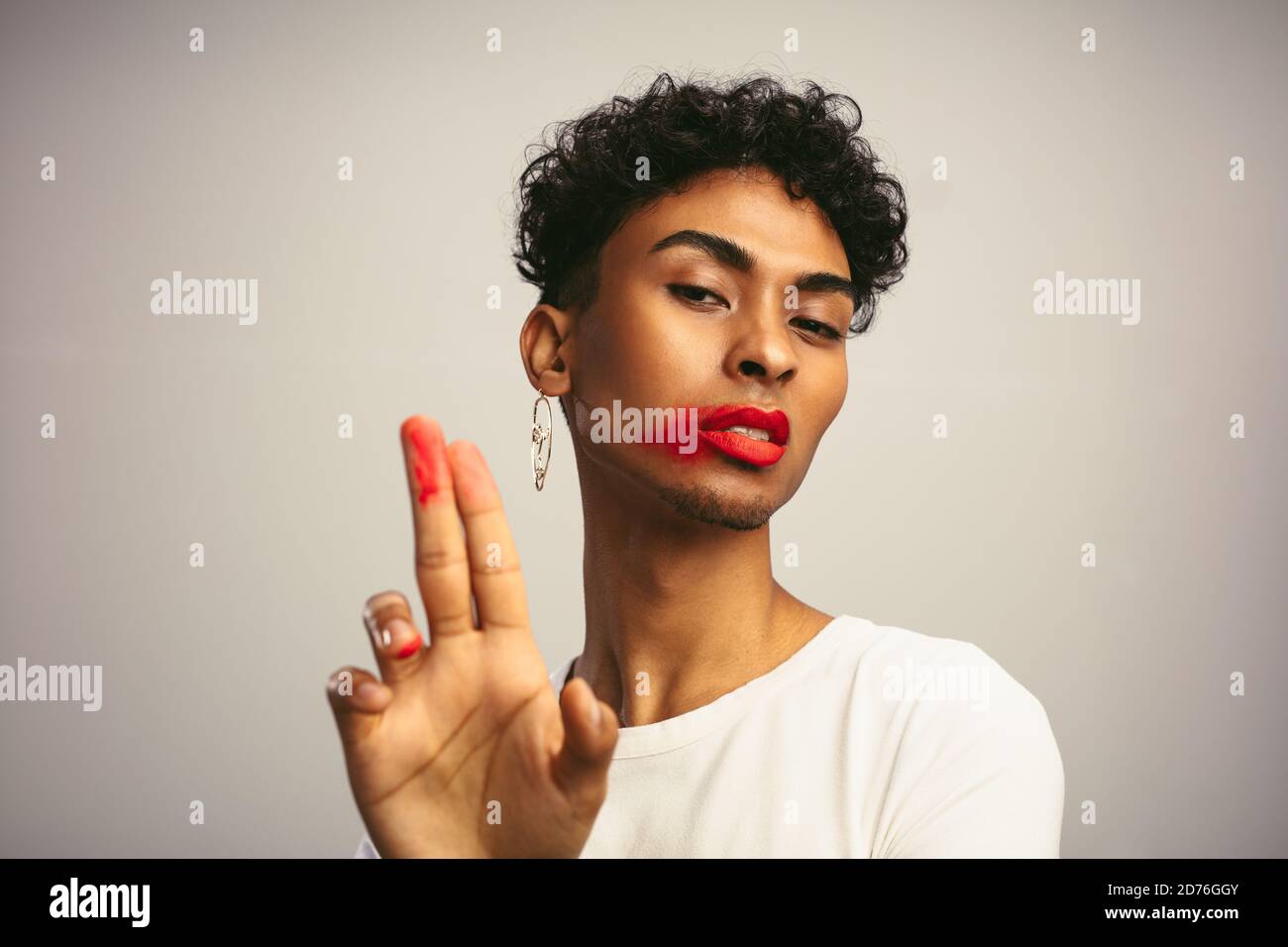 Homme androgyne montrant ses doigts après avoir enduit son rouge à lèvres . Homme transgenre avec rouge à lèvres soumpé regardant l'appareil photo. Banque D'Images
