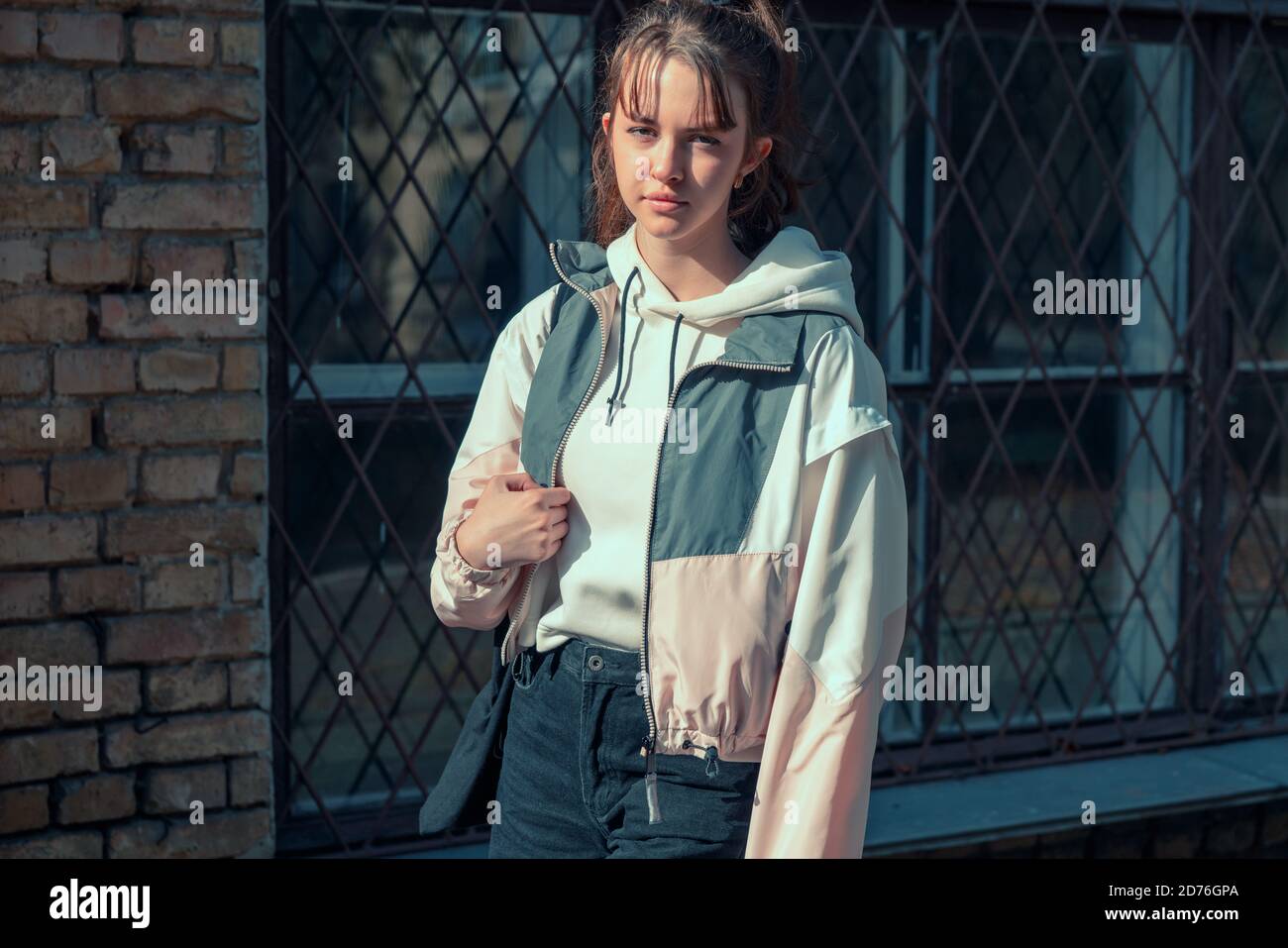 Une jeune adolescente sérieuse et réfléchie debout avec un sac de livre sur son épaule devant un bâtiment urbain regarder l'appareil photo en silence Banque D'Images