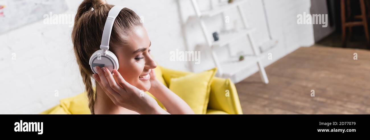 Photo panoramique d'une jeune femme souriant tout en écoutant de la musique des écouteurs à la maison Banque D'Images