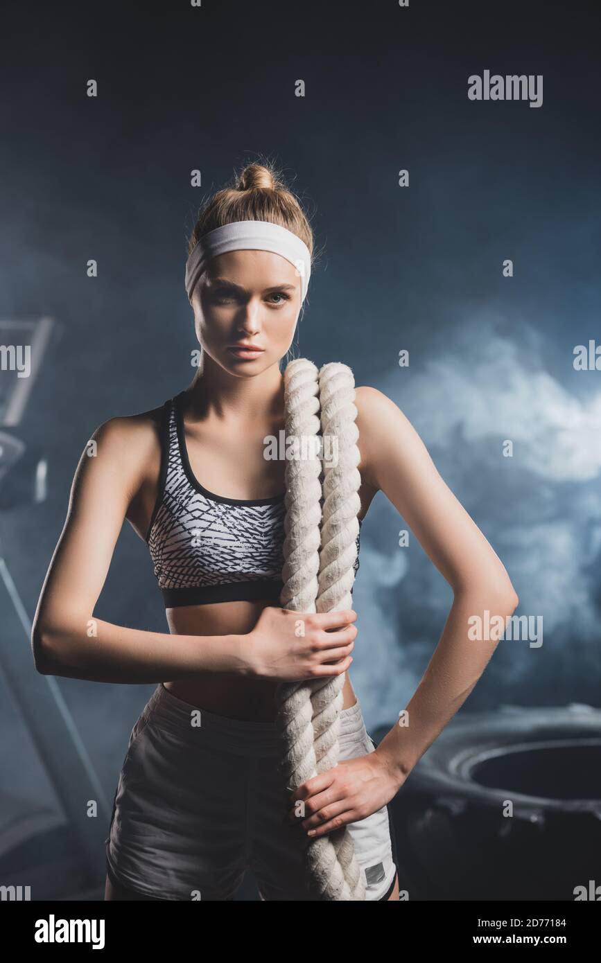 Jeune sportswoman avec corde de bataille regardant la caméra dans le sport centre avec fumée Banque D'Images
