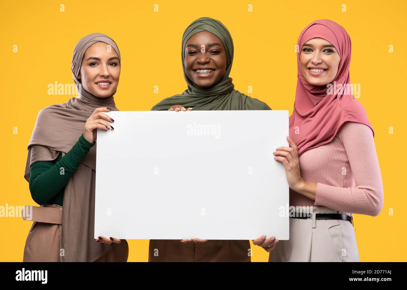 Trois musulmanes tenant une affiche vide sur fond jaune Banque D'Images