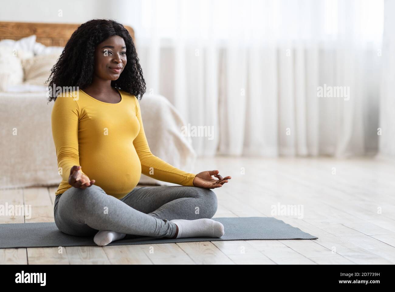 Femme africaine enceinte méditant en position de lotus à la maison Banque D'Images