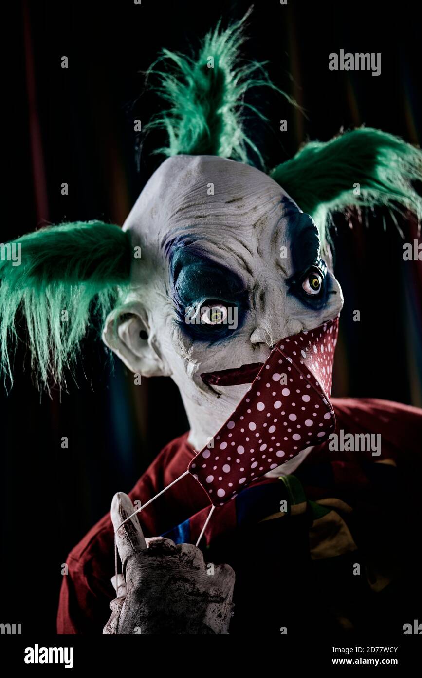 gros plan d'un clown maléfique troublant, avec des cheveux verts, portant un costume rouge sale, une cravate sale, et des gants sales et sanglants, mettant sur ou prenant o Banque D'Images
