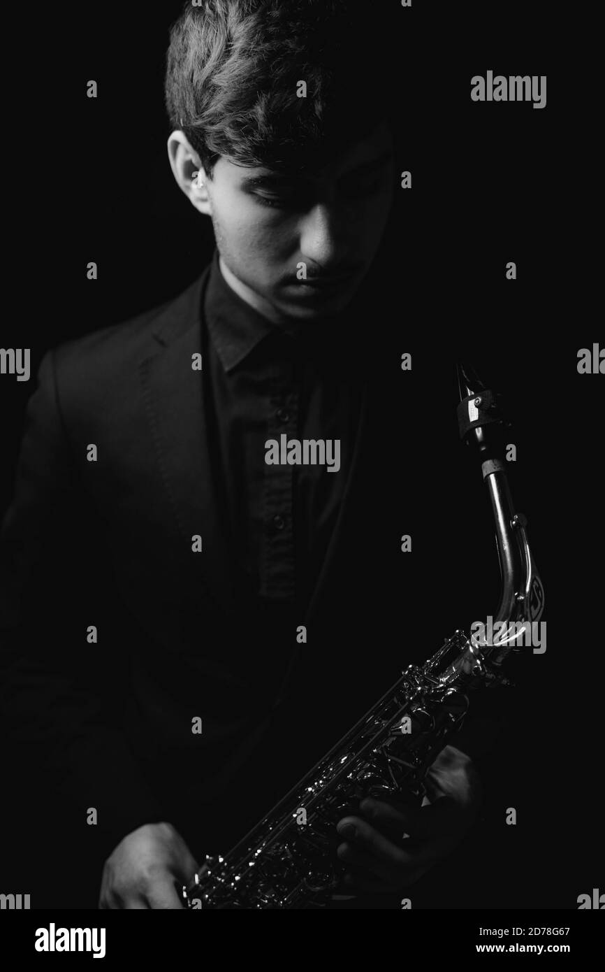 Prise de vue en niveaux de gris d'un gars sympa et charmant tenant son saxophone sur fond sombre Banque D'Images