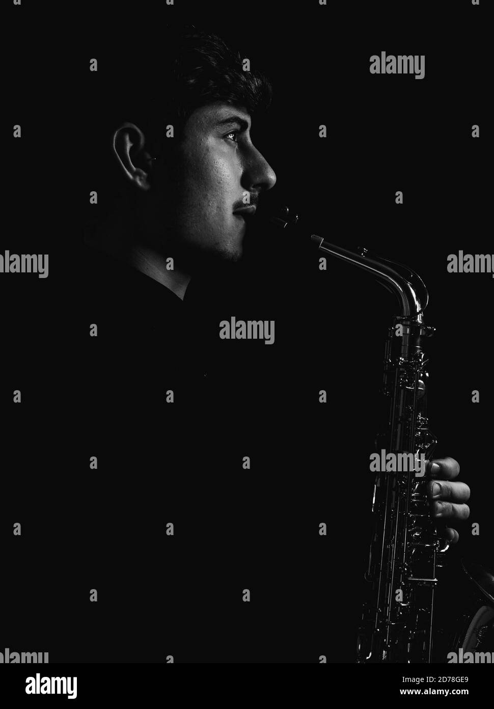 Prise de vue en niveaux de gris d'un gars sympa et charmant jouant son saxophone isolé sur fond sombre Banque D'Images