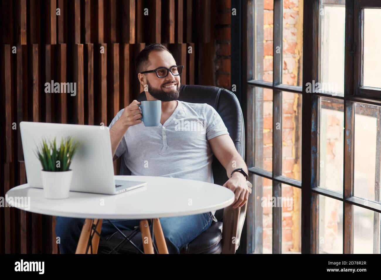Jeune homme d'affaires barbu avec succès freelance dans un collègue de bureau. Happy man programmeur développeur dans un t-shirt blanc souriant et buvant du café à Banque D'Images