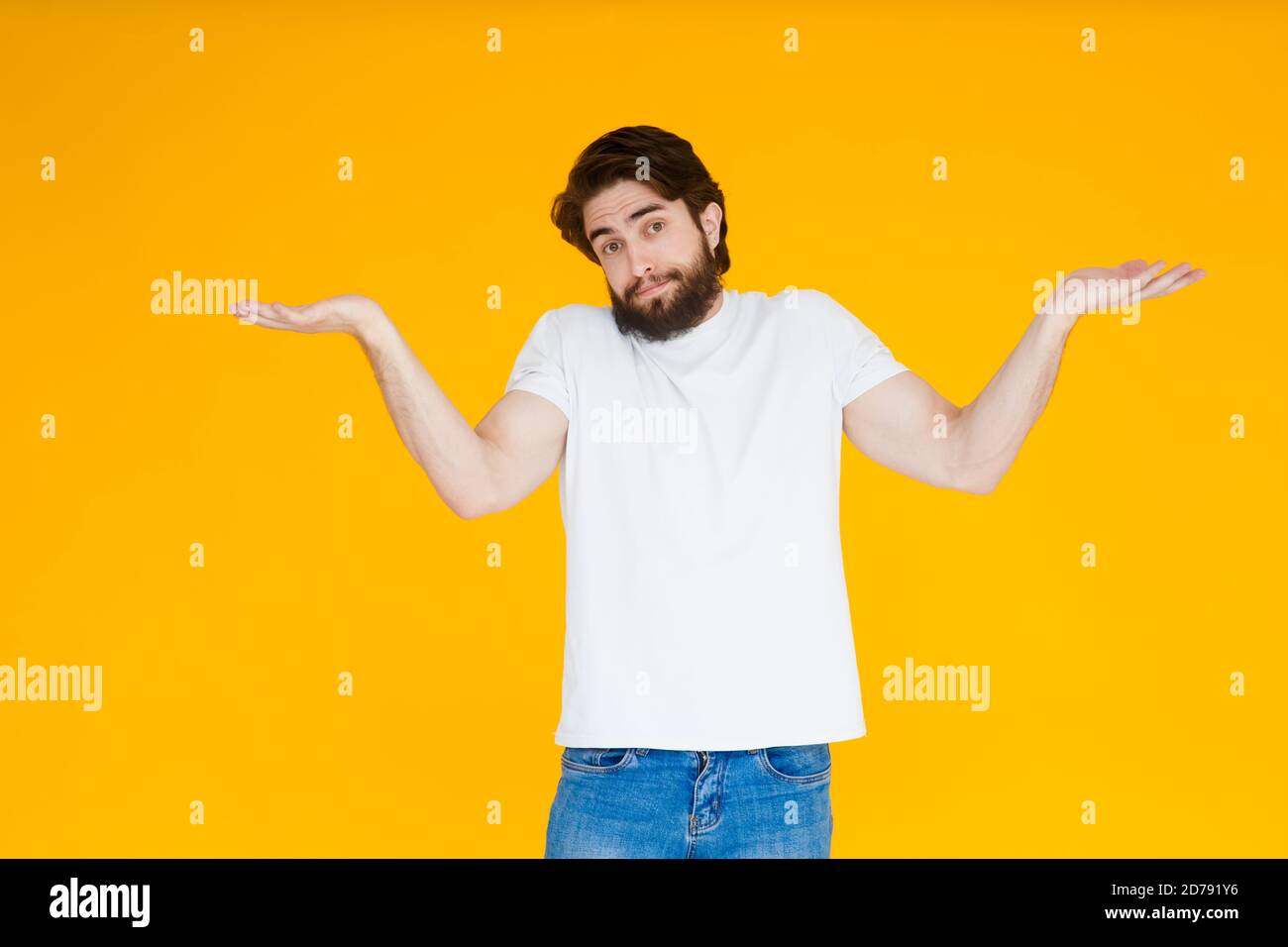 Un jeune homme avec une barbe dans un T-shirt blanc écartant ses bras, choqué par l'expression inattendue, hésite à dire, la réponse n'a aucune idée. JE Banque D'Images