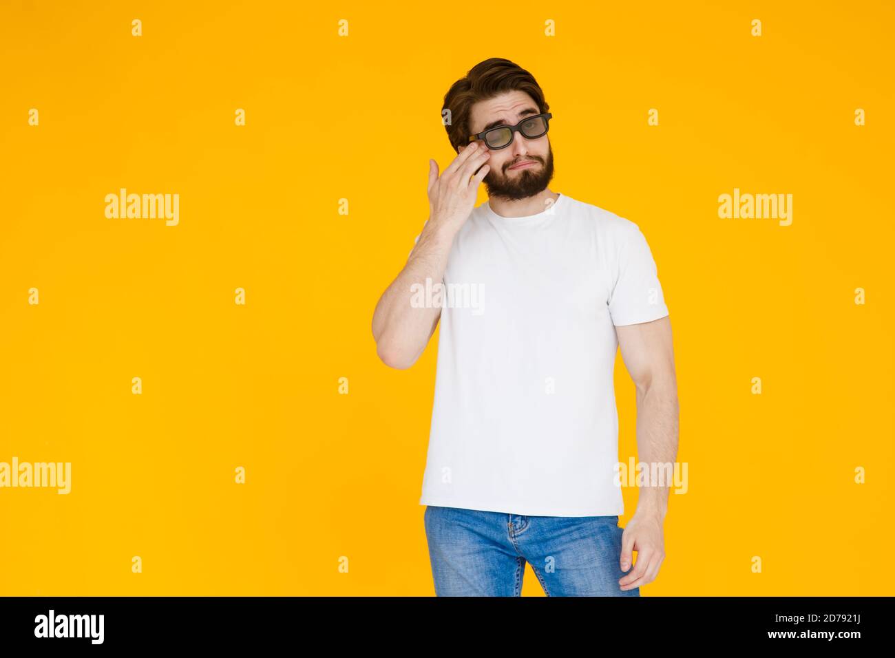 Jeune homme barbu dans un t-shirt blanc avec 3D les lunettes regardent un film mélodrame sur fond jaune Banque D'Images
