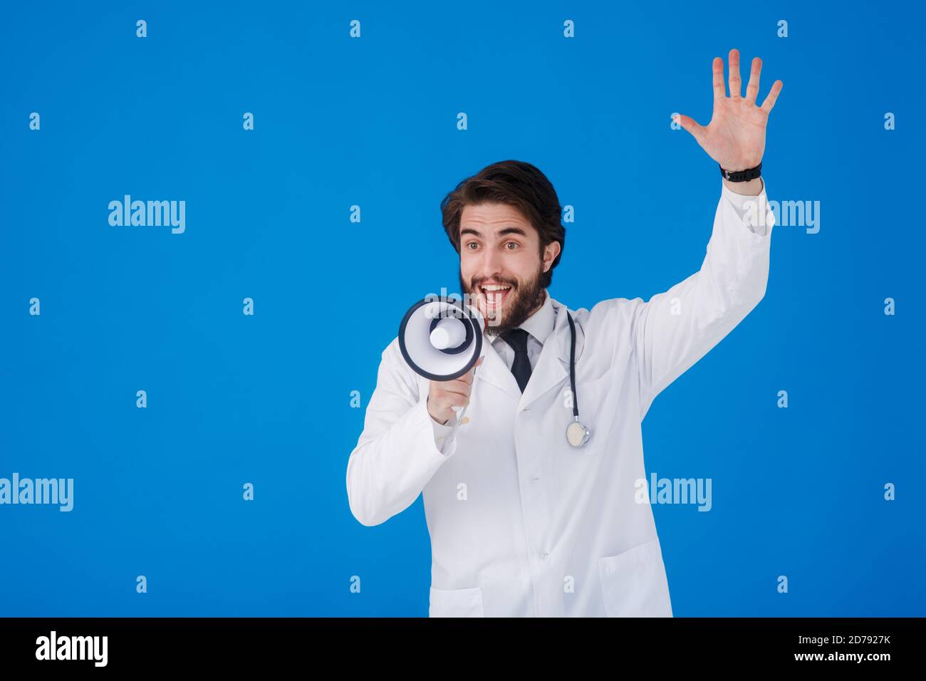 un jeune barbu médecin sur fond bleu avec un le mégaphone entre ses mains criait Banque D'Images