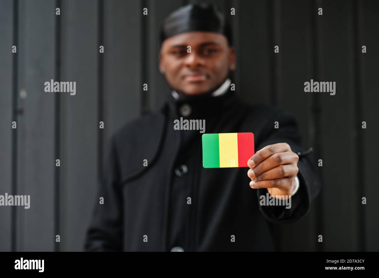 L'homme africain porte du durag noir tient le drapeau du Mali à la main isolé arrière-plan sombre. Banque D'Images