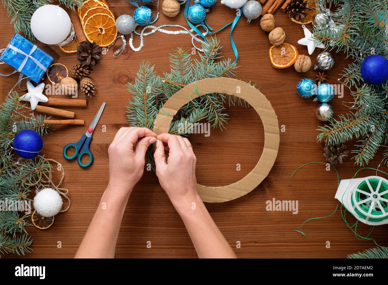 Processus étape par étape de fabrication d'une couronne d'arbre de Noël à la maison à partir de branches d'épinette, d'oranges et de boules de Noël dans les couleurs argent et bleu de la Banque D'Images