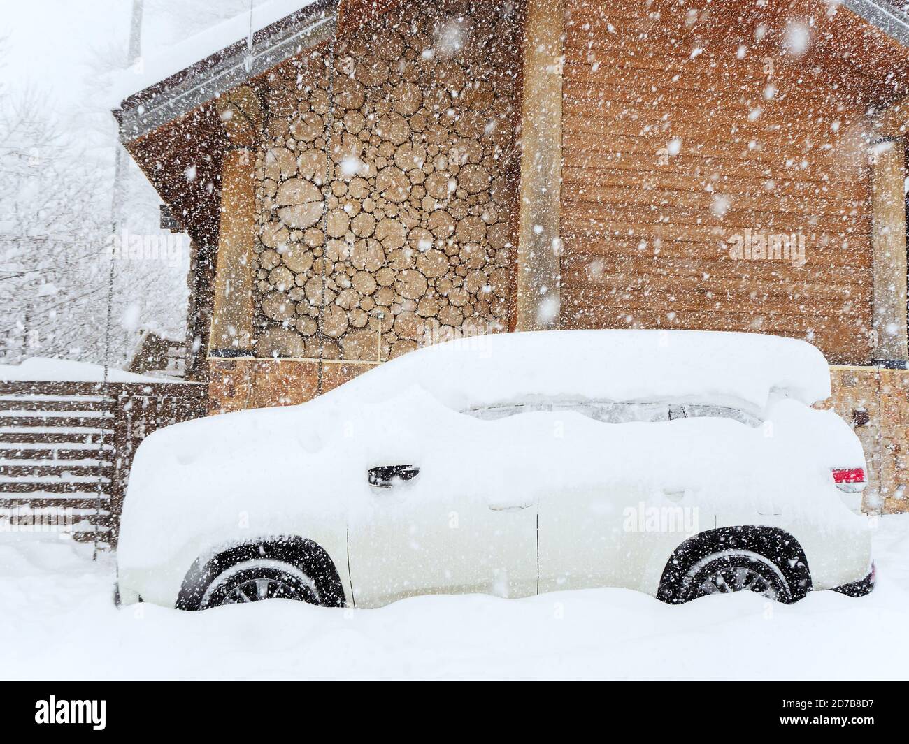 Une voiture enneigée est garée près d'une cabane en bois une journée nuageux avec de la neige épaisse Banque D'Images