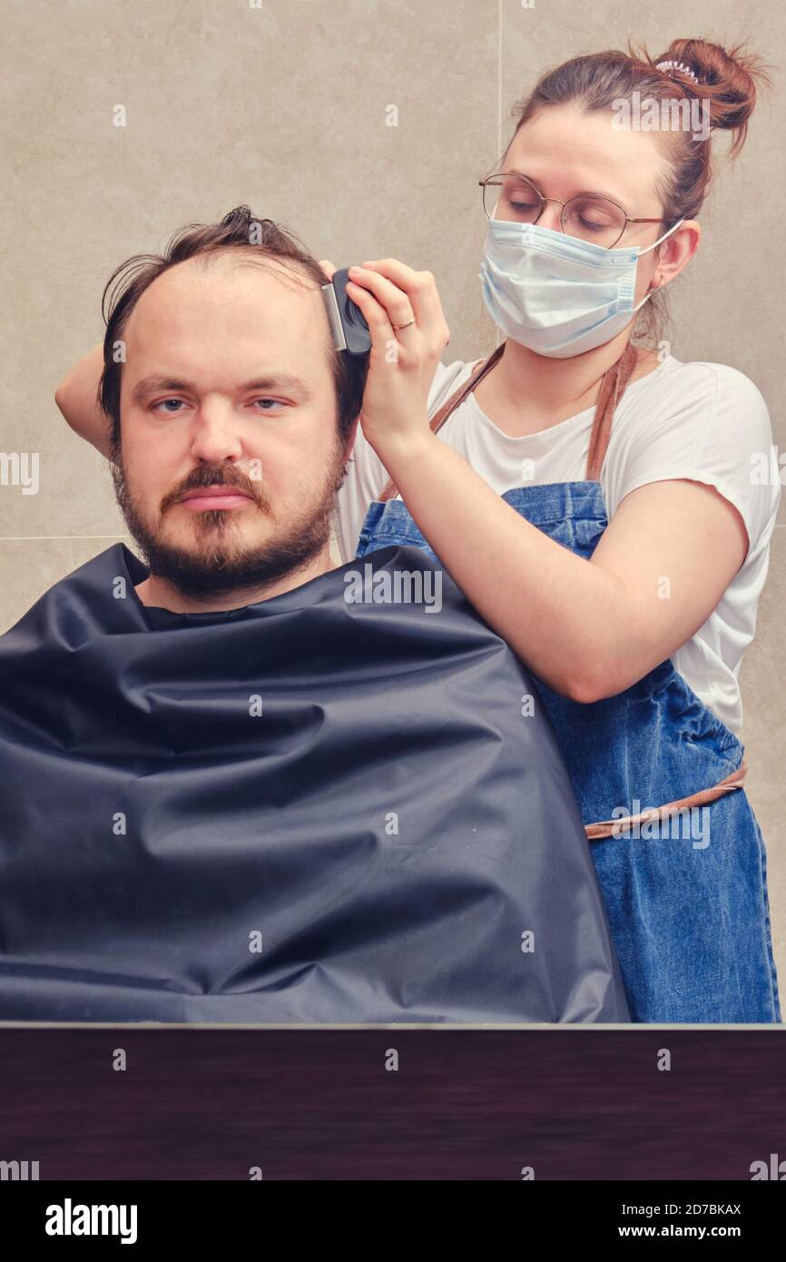 Une femme avec une tondeuse coupe les cheveux de son mari dans la salle de  bains avec miroir, espace de copie. Concept d'auto-coupure et de rasage  pendant l'épidémie de grippe Photo Stock -