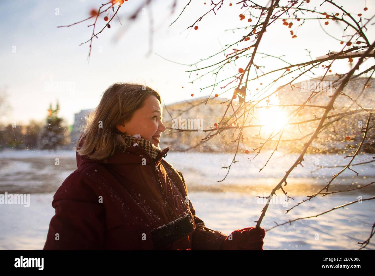 Activités saisonnières en hiver. Belle femme jetant de la neige dans l'air au coucher du soleil en tenant des branches d'arbre. Banque D'Images