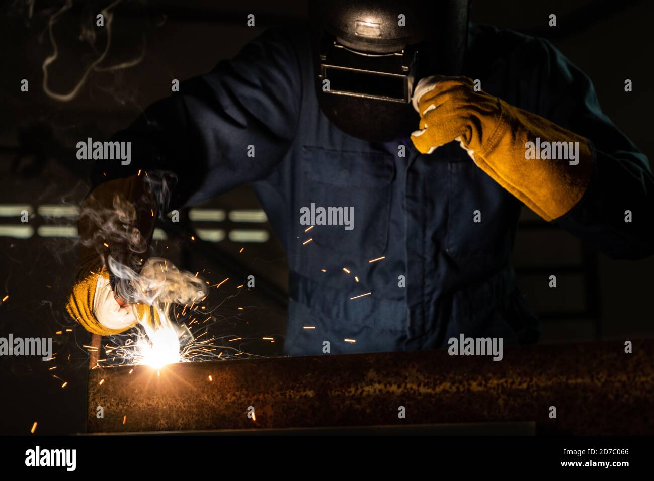 Soudeur de métal travaillant avec une machine à souder à l'arc pour souder l'acier en usine tout en portant un équipement de sécurité. Fabrication et construction de métaux Banque D'Images
