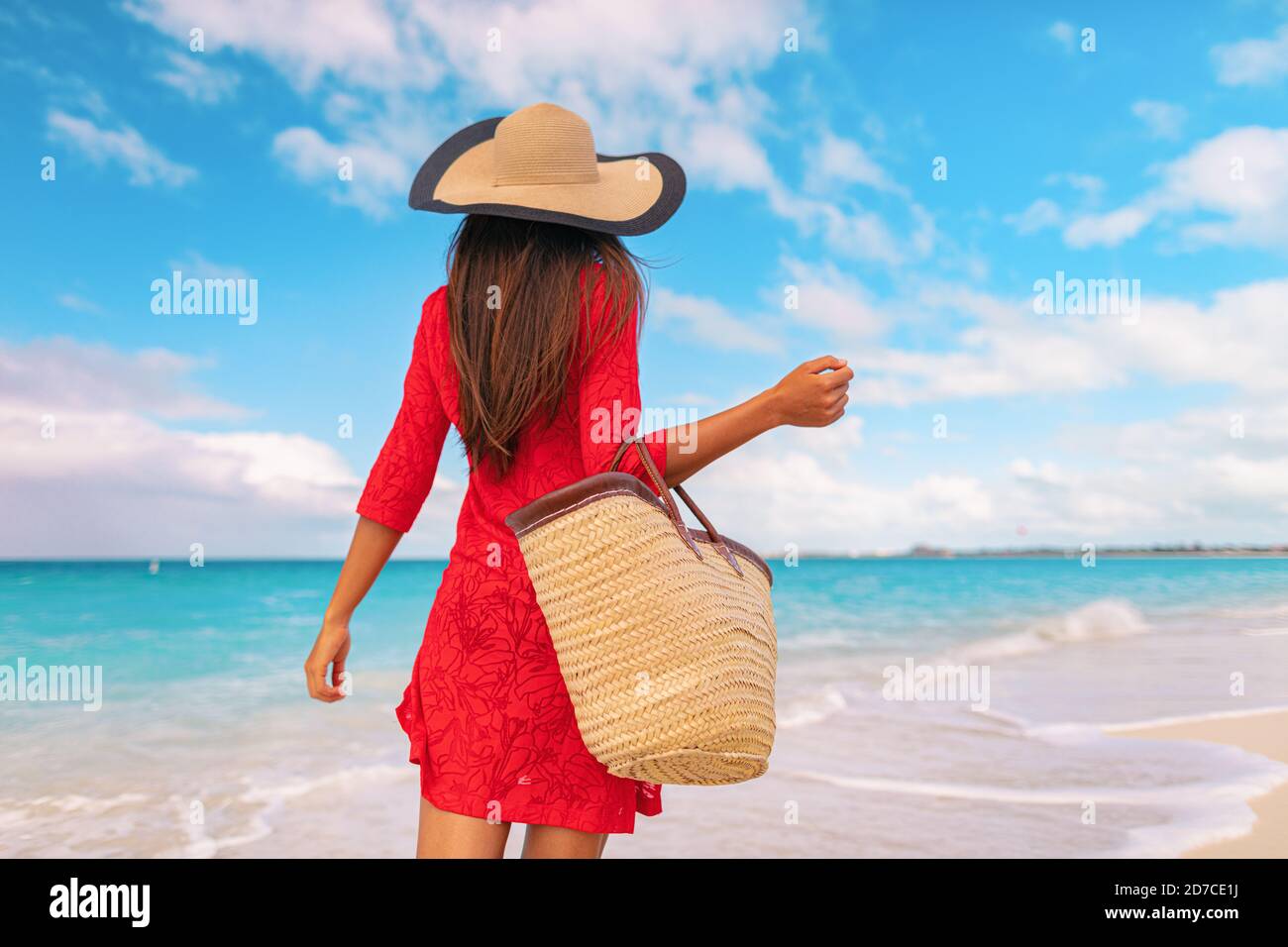 Femme touriste marchant sur les vacances tropicales d'été portant un chapeau  de soleil, robe rouge et sac de plage relaxant sur les vacances de voyage.  Jeune femme de derrière Photo Stock -