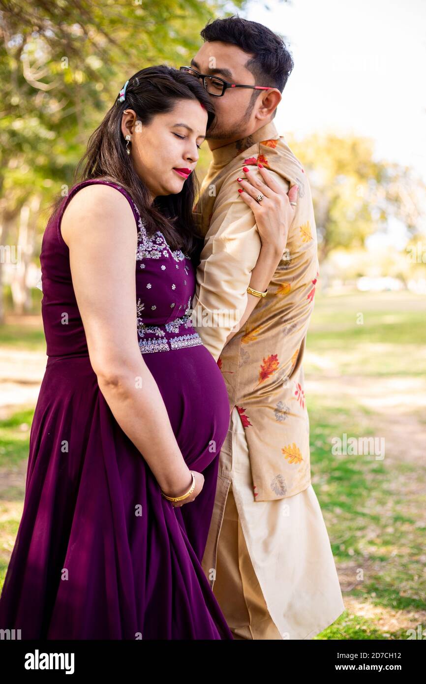 Jeune femme enceinte asiatique indienne avec son mari portant une tenue traditionnelle debout dans un parc ou un jardin pour écrire du texte. Banque D'Images
