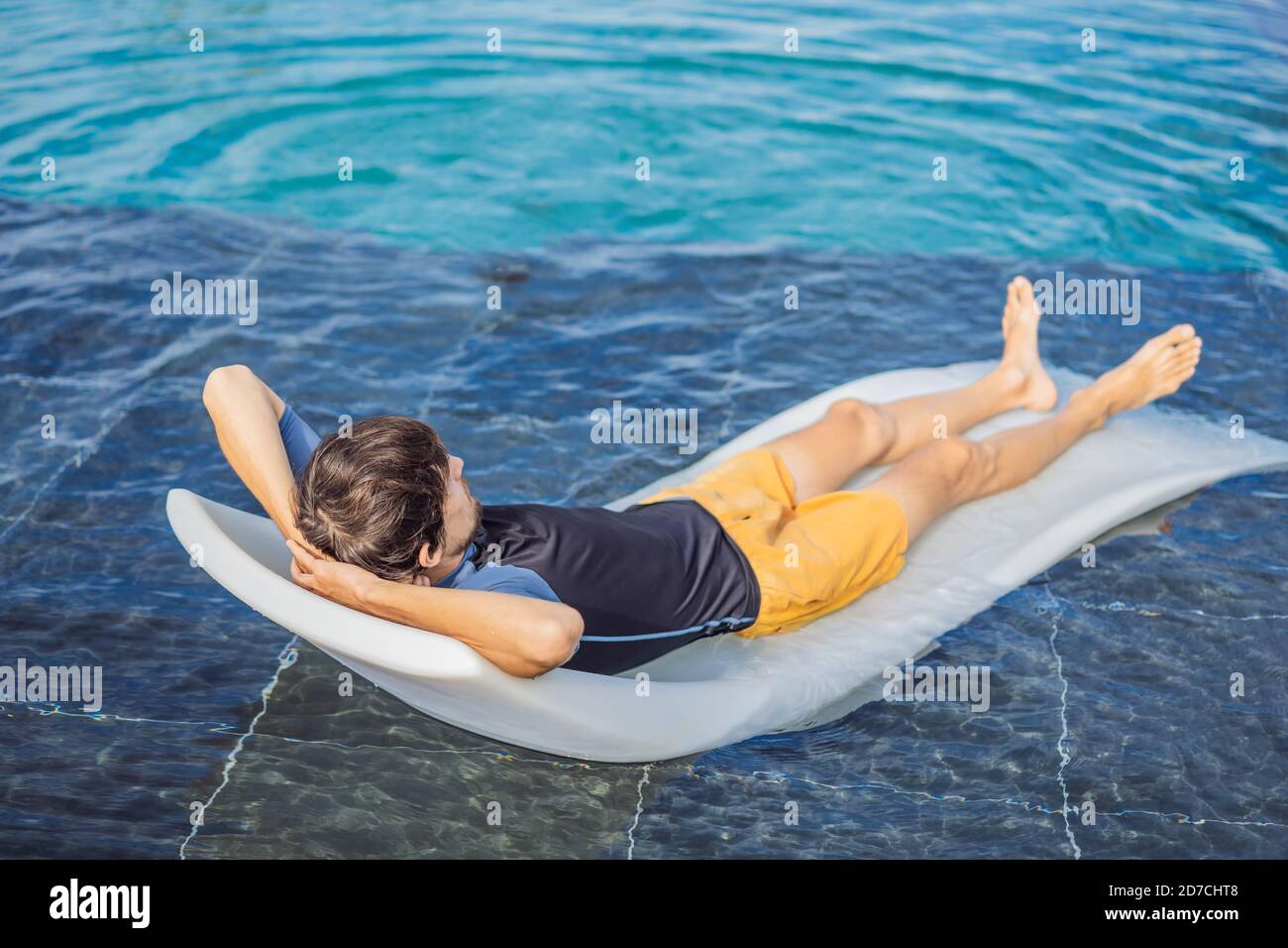 Détendez-vous dans la piscine. Jeune homme réussi allongé sur un transat et des tans dans la piscine de l'hôtel Banque D'Images