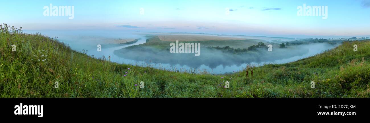 Magnifique paysage brumeux froid d'été avec creux brumeux avec rivière calme et collines vertes avant le lever du soleil. Banque D'Images