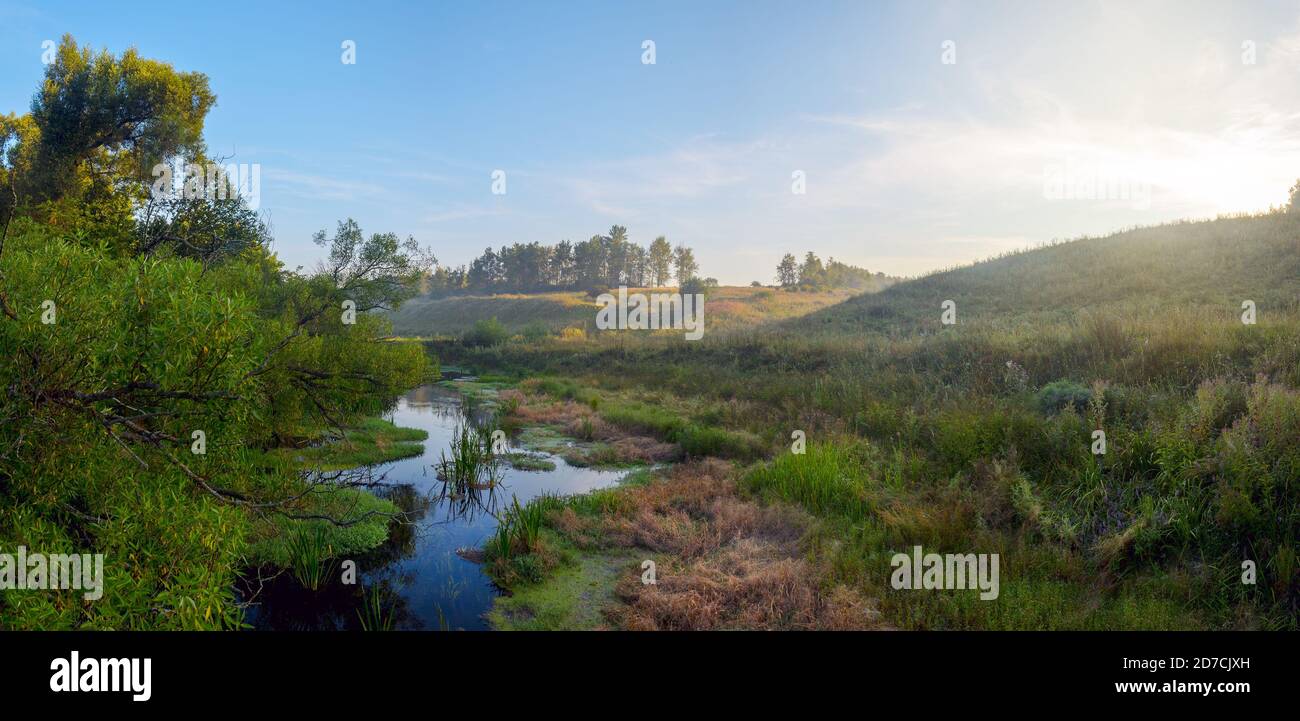 Paysage paisible et brumeux avec petite rivière au lever du soleil Banque D'Images