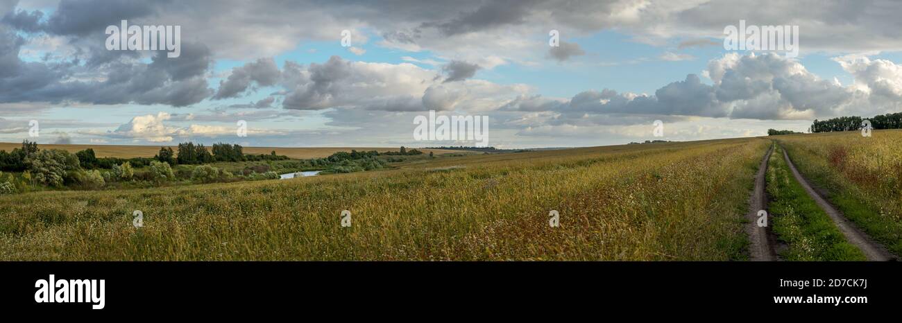 Paysage panoramique d'été avec route rurale et nuages noirs de pluie sur les champs de la ferme Banque D'Images