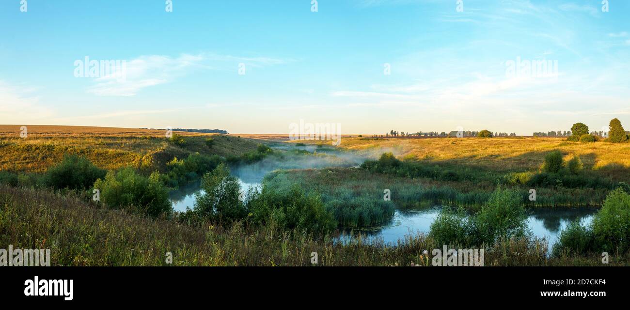 Vue panoramique sur une rivière calme pendant un lever de soleil brumeux. Banque D'Images