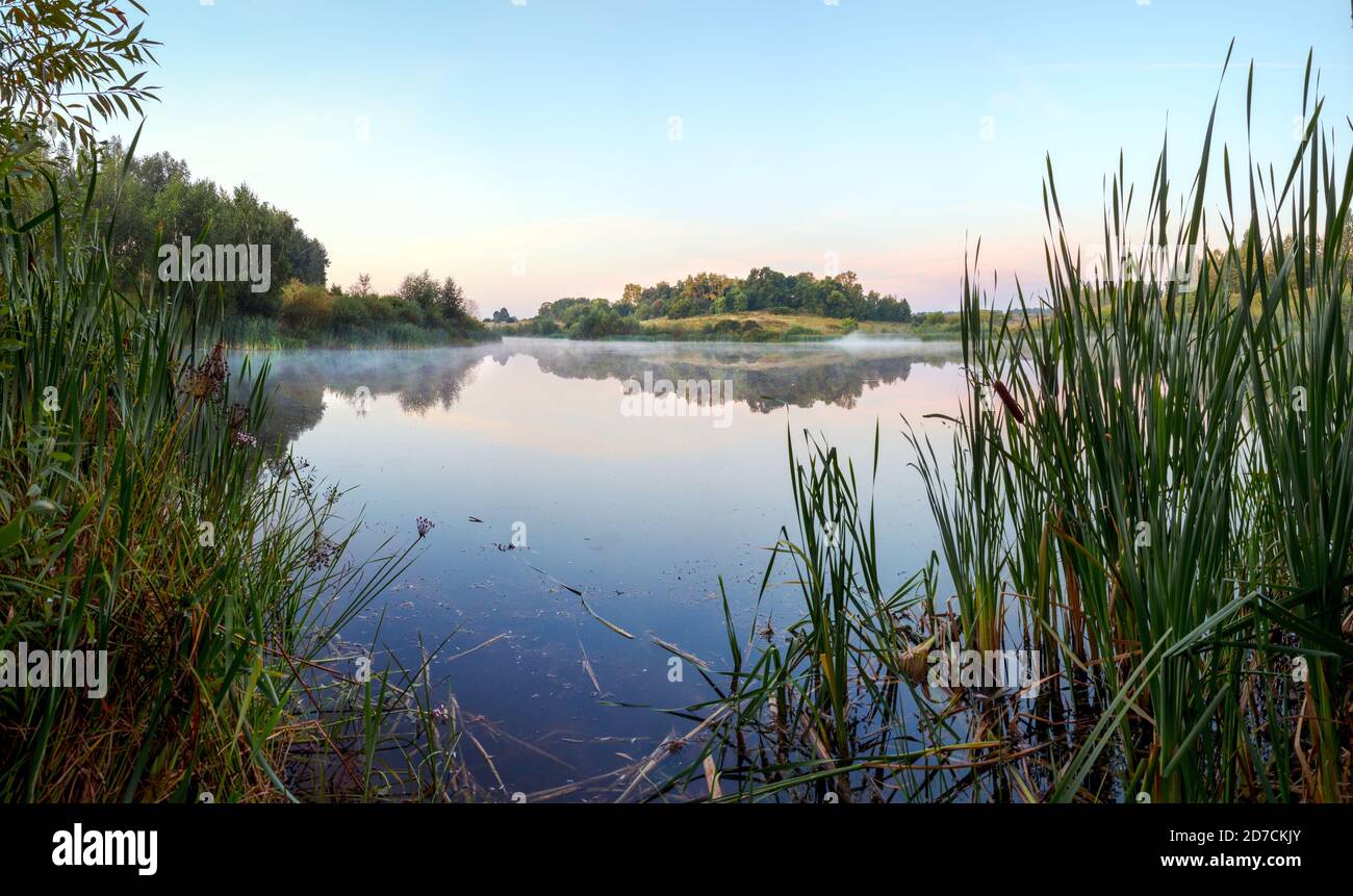 Vue panoramique sur le lac calme pendant le lever du soleil brumeux. Banque D'Images