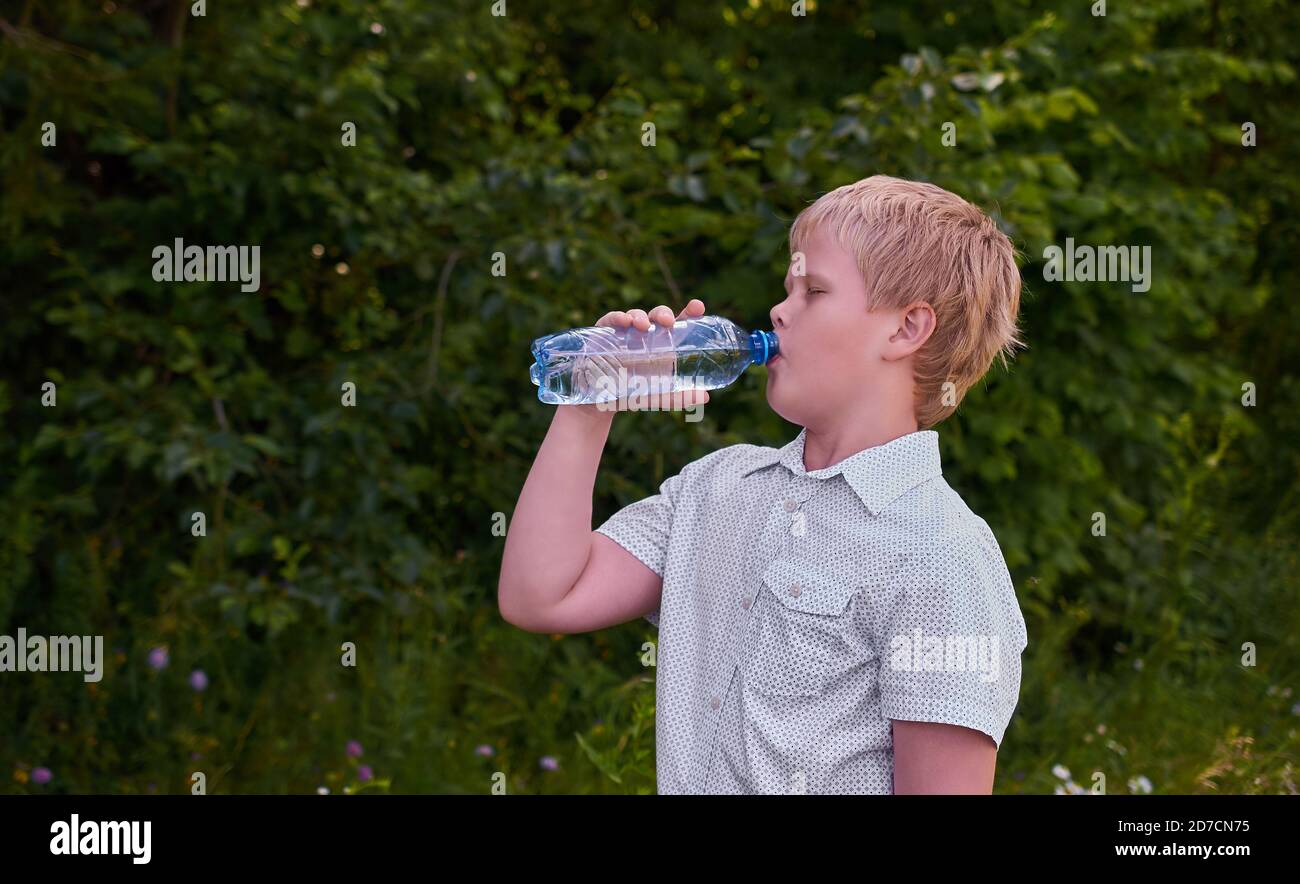 Un garçon boit de l'eau d'une bouteille en plastique sur un Promenade dans le parc en été Banque D'Images