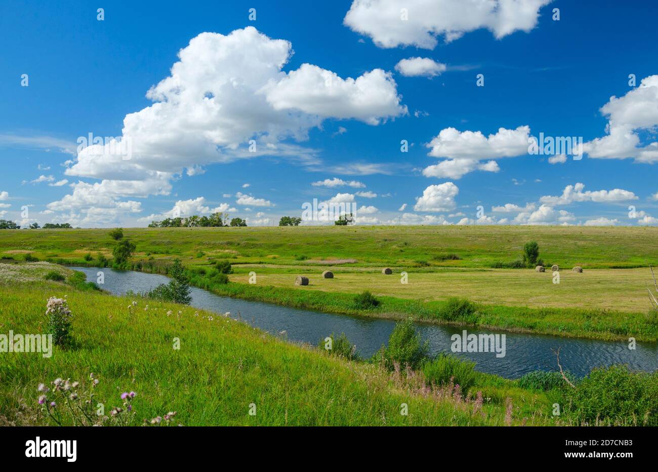 Paysage ensoleillé d'été avec rivière, collines vertes et de beaux nuages dans le ciel bleu. Banque D'Images