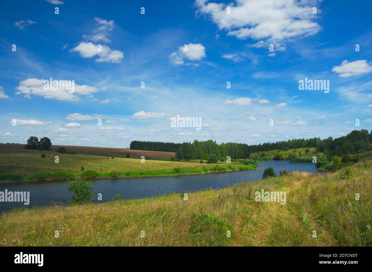 Paysage ensoleillé d'été avec rivière, collines vertes et de beaux nuages dans le ciel bleu. Banque D'Images