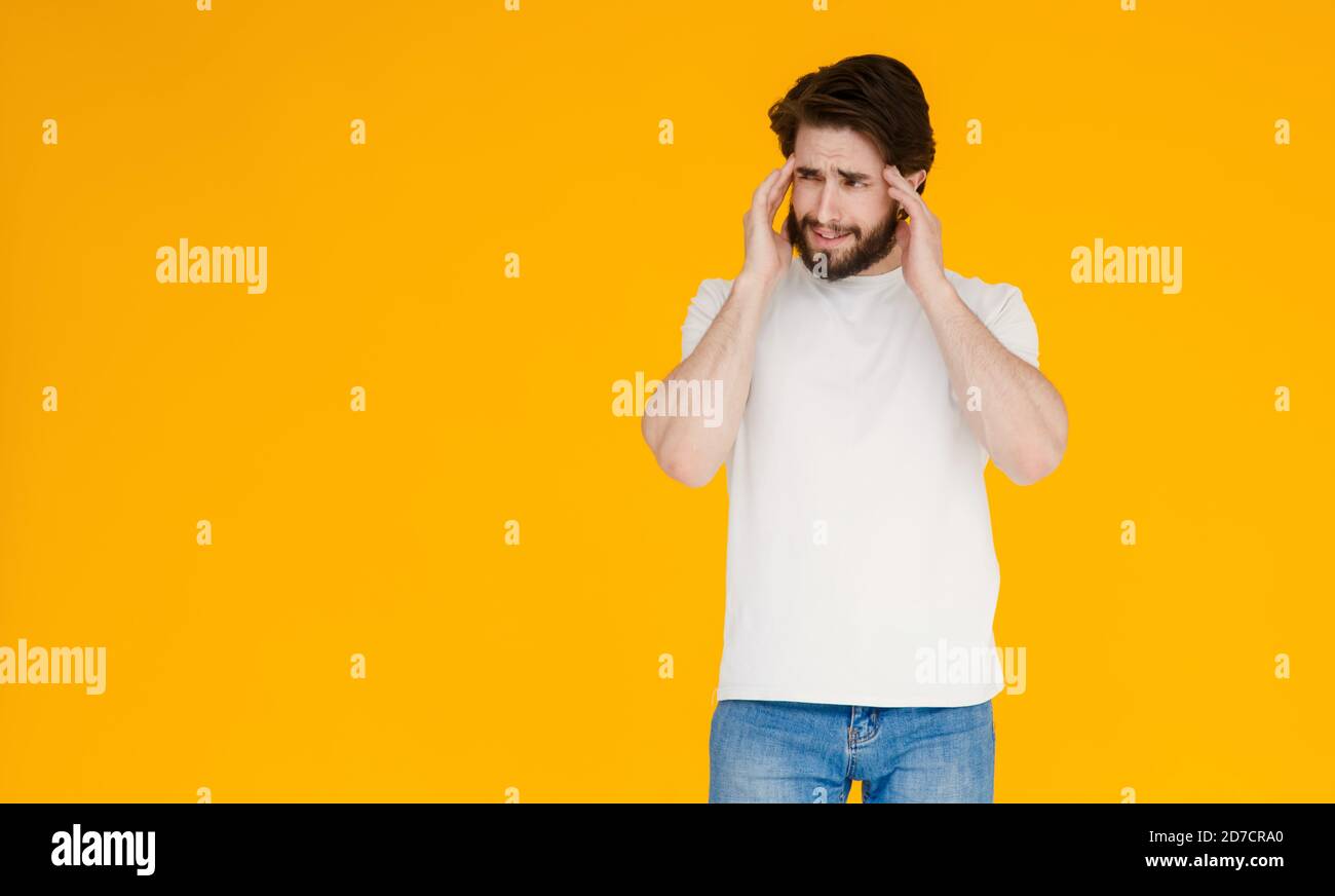 Un jeune homme barbu dans un t-shirt blanc sur fond jaune. Le concept de tension , de mal de tête et de fatigue Banque D'Images