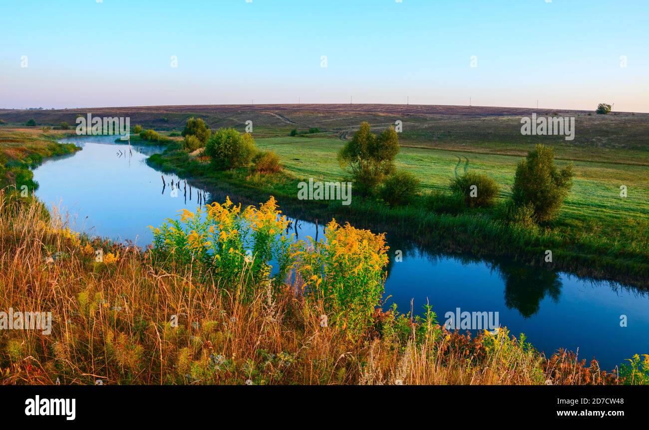 Paysage ensoleillé d'été avec rivière qui coule entre les belles collines verdoyantes, les champs et les prairies. Banque D'Images