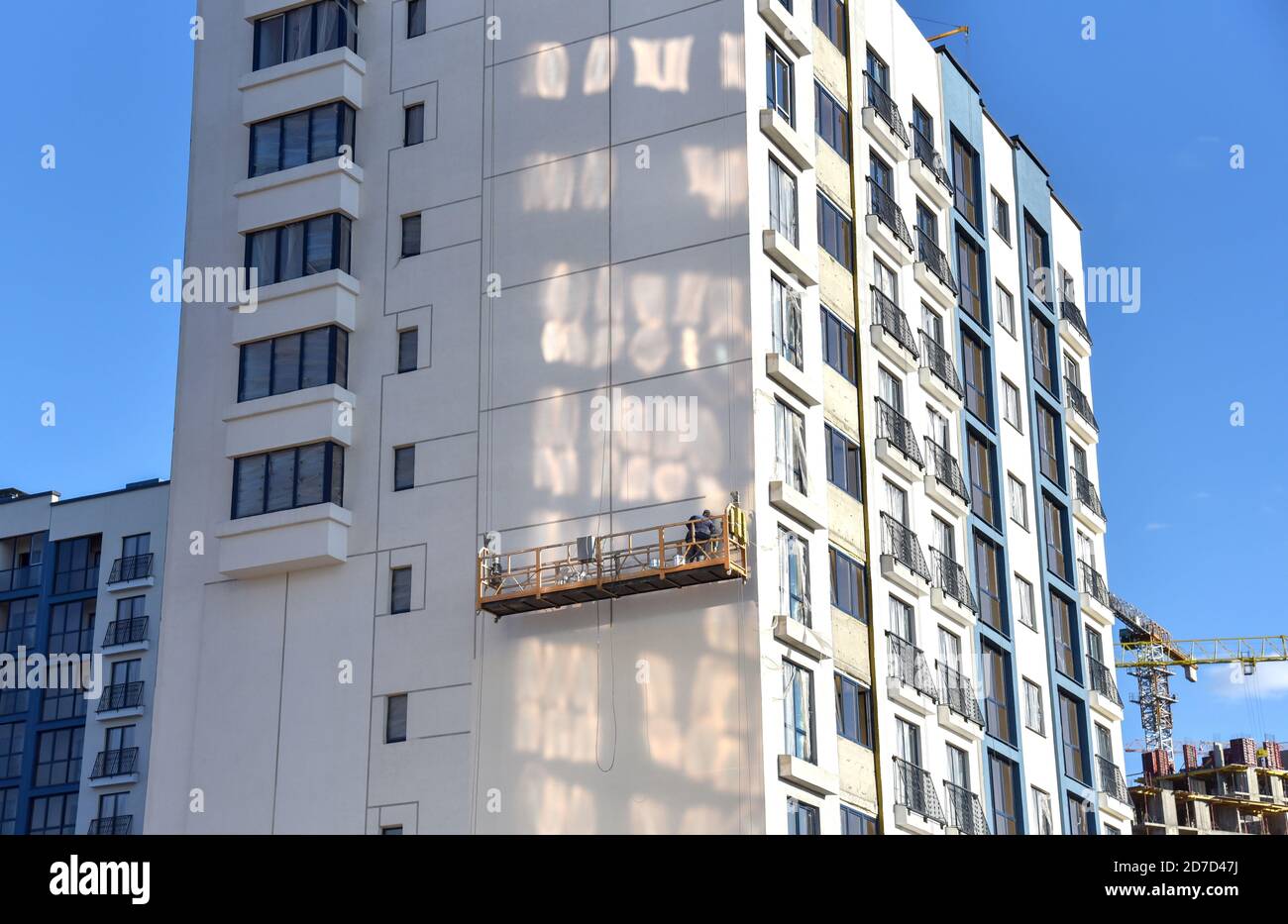 Un constructeur sur un berceau suspendu peint la casaque d'un nouveau bâtiment résidentiel. Plate-forme d'échafaudage mobile pour les travaux de construction en hauteur. Banque D'Images