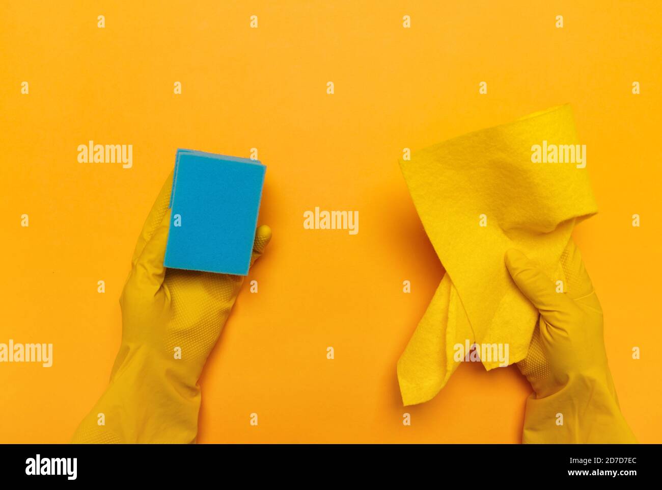 mains dans des gants jaunes en caoutchouc tenir un chiffon jaune et une éponge bleue sur un fond jaune. placer pour le texte. Banque D'Images