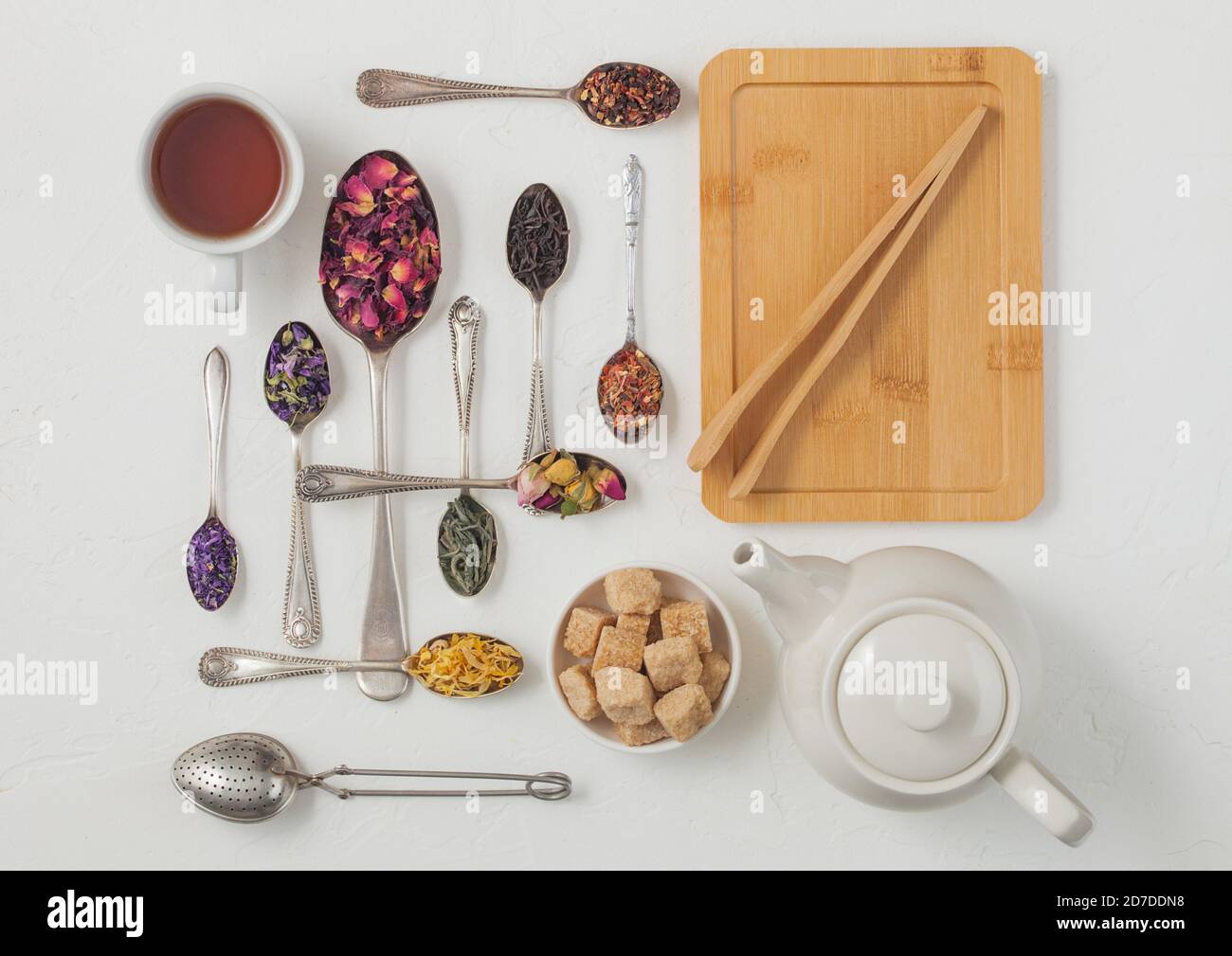 Cuillères avec différents classiques et tisanes sur fond blanc avec théière et tasse, planche en bois et infuser passoire vintage. Vue de dessus Banque D'Images