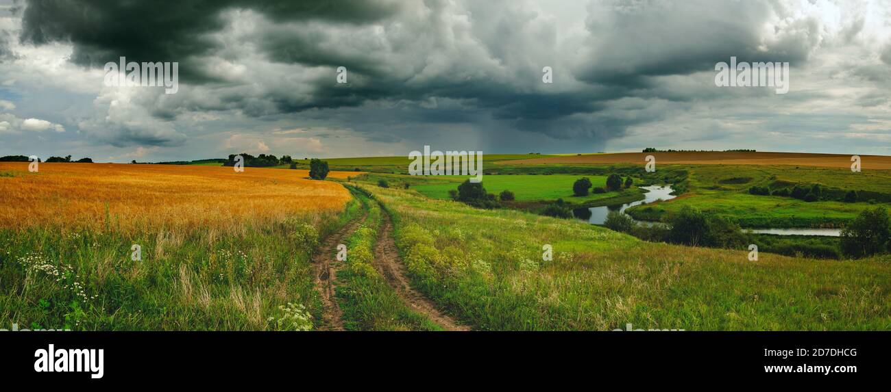 Paysage panoramique d'été nuageux avec route de campagne de terre, champs et petite rivière. Banque D'Images