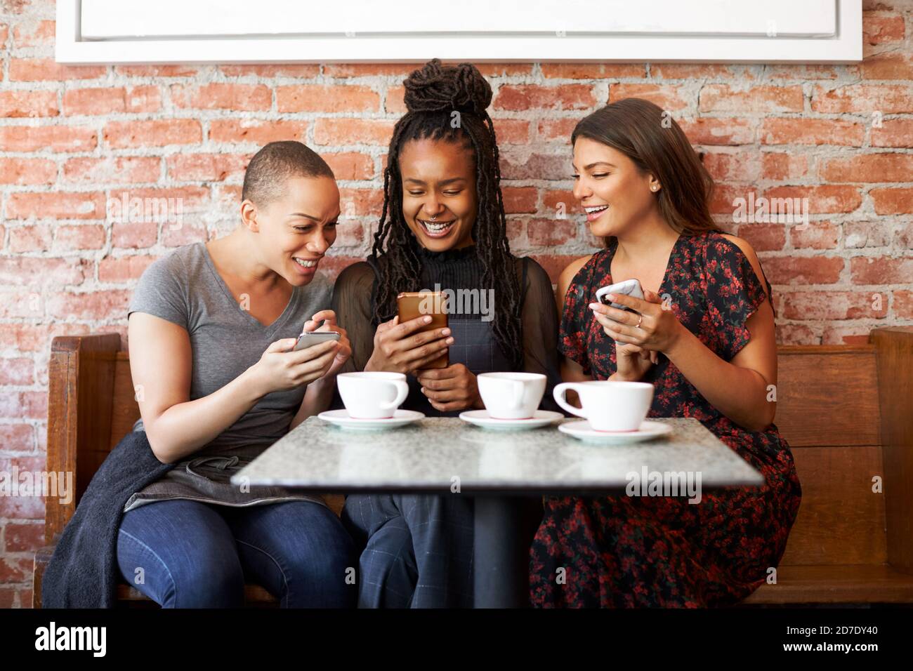 Trois rencontres d'amis féminins pour un café assis à la table Sur les téléphones mobiles Banque D'Images