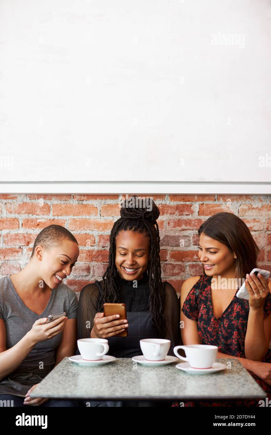 Trois rencontres d'amis féminins pour un café assis à la table Sur les téléphones mobiles Banque D'Images