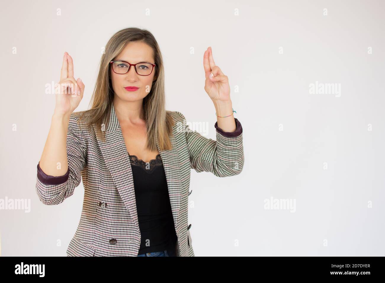 Jeune jolie femme qui croise avec inquiétude les deux doigts, se sentant inquiète et souhaitant ou espérant bonne chance contre le mur blanc Banque D'Images
