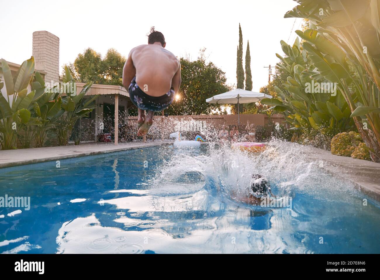 Les femmes se détendent à l'extérieur lors d'une fête d'été en bord de piscine en regardant les hommes plonger Dans l'eau Banque D'Images