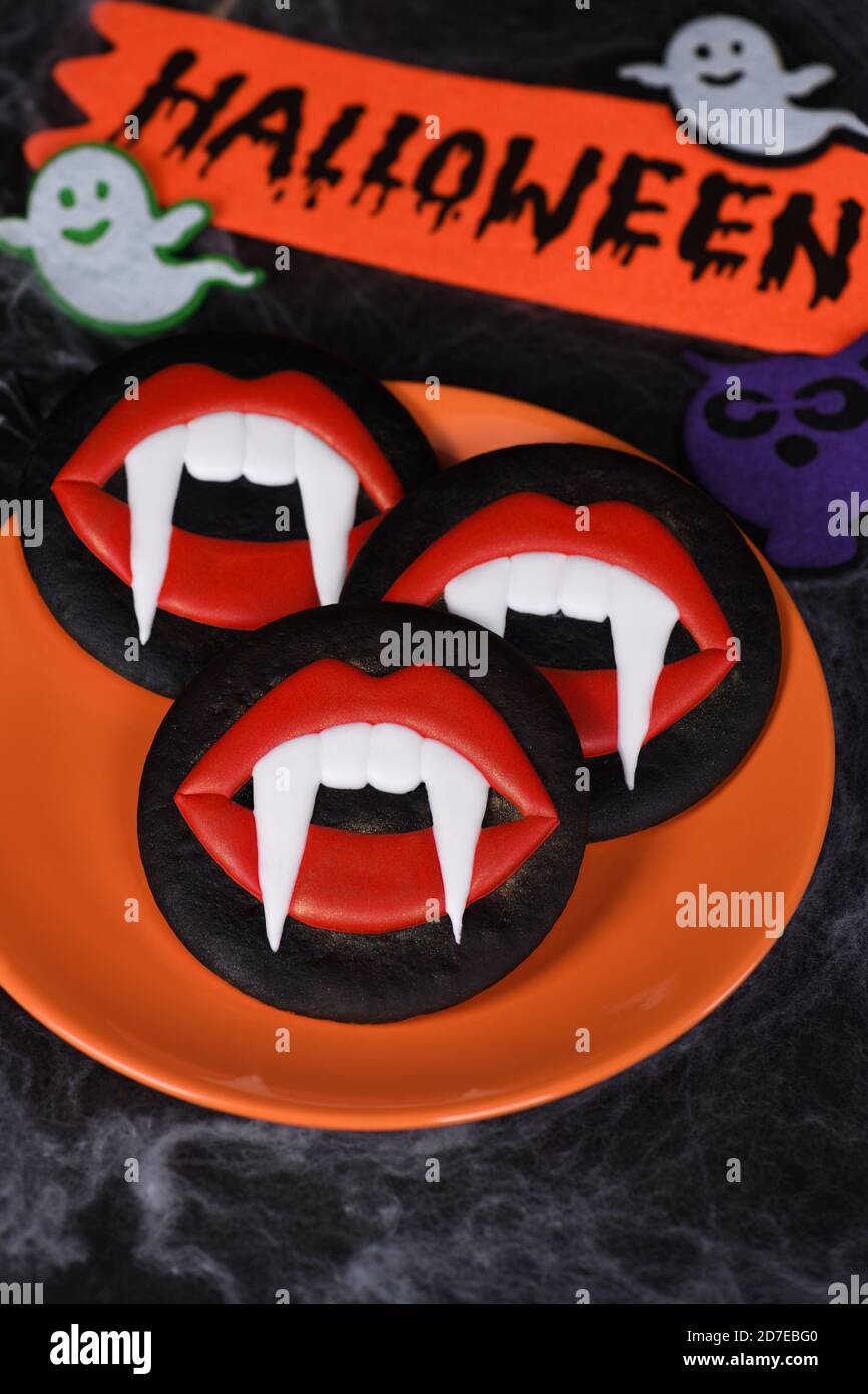 Fangs de vampire dépassant des lèvres de scarlet, biscuits glacés de pain d'épice au miel. Idée de nourriture pour Halloween Banque D'Images