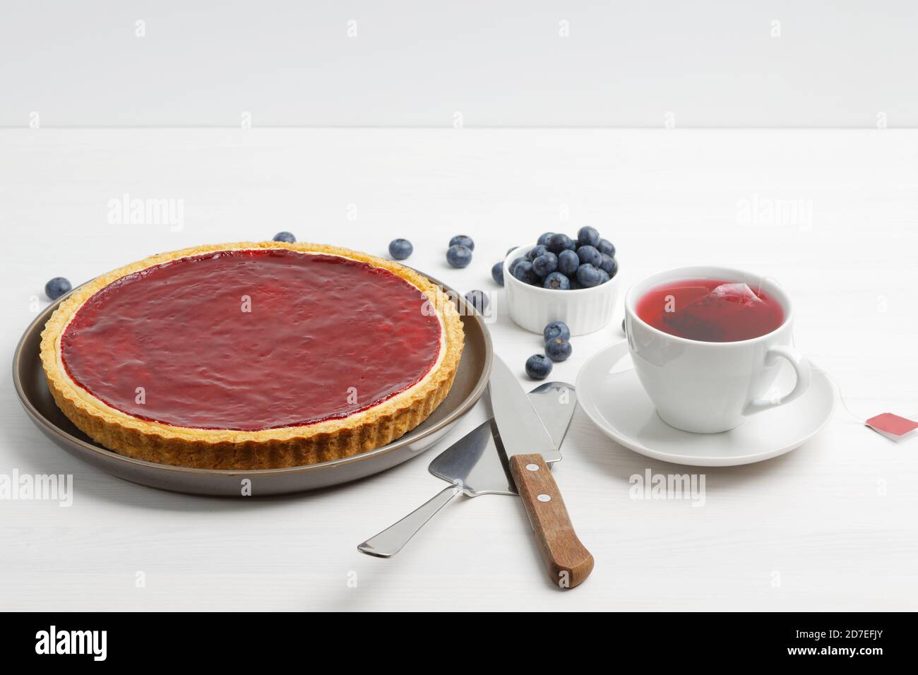 Cheesecake maison avec gelée de baies et une tasse d'hibiscus de thé rouge sur une table en bois blanc. Banque D'Images