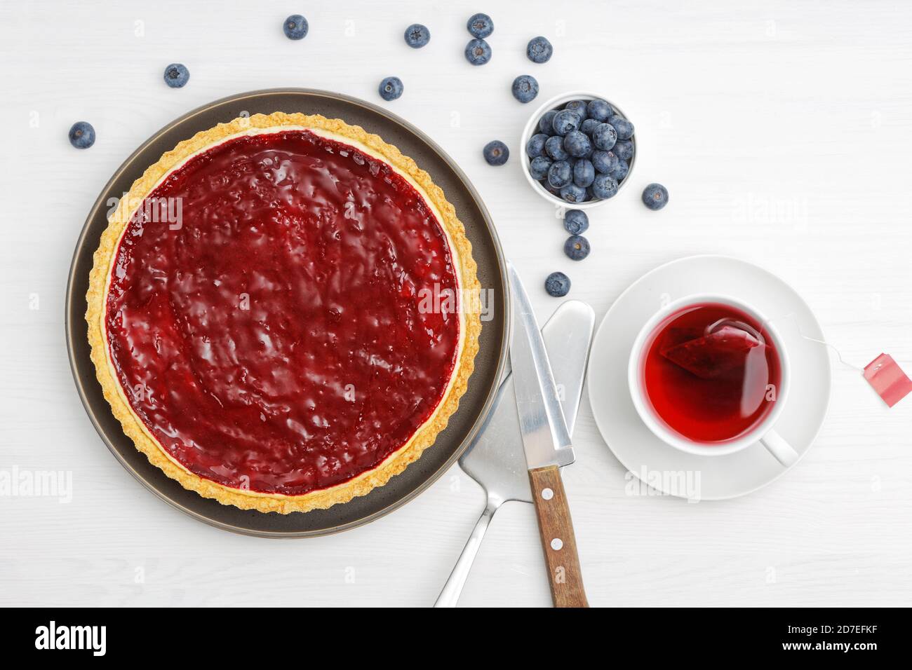 Cheesecake maison avec gelée de baies et une tasse d'hibiscus de thé rouge sur une table en bois blanc. Vue de dessus. Banque D'Images