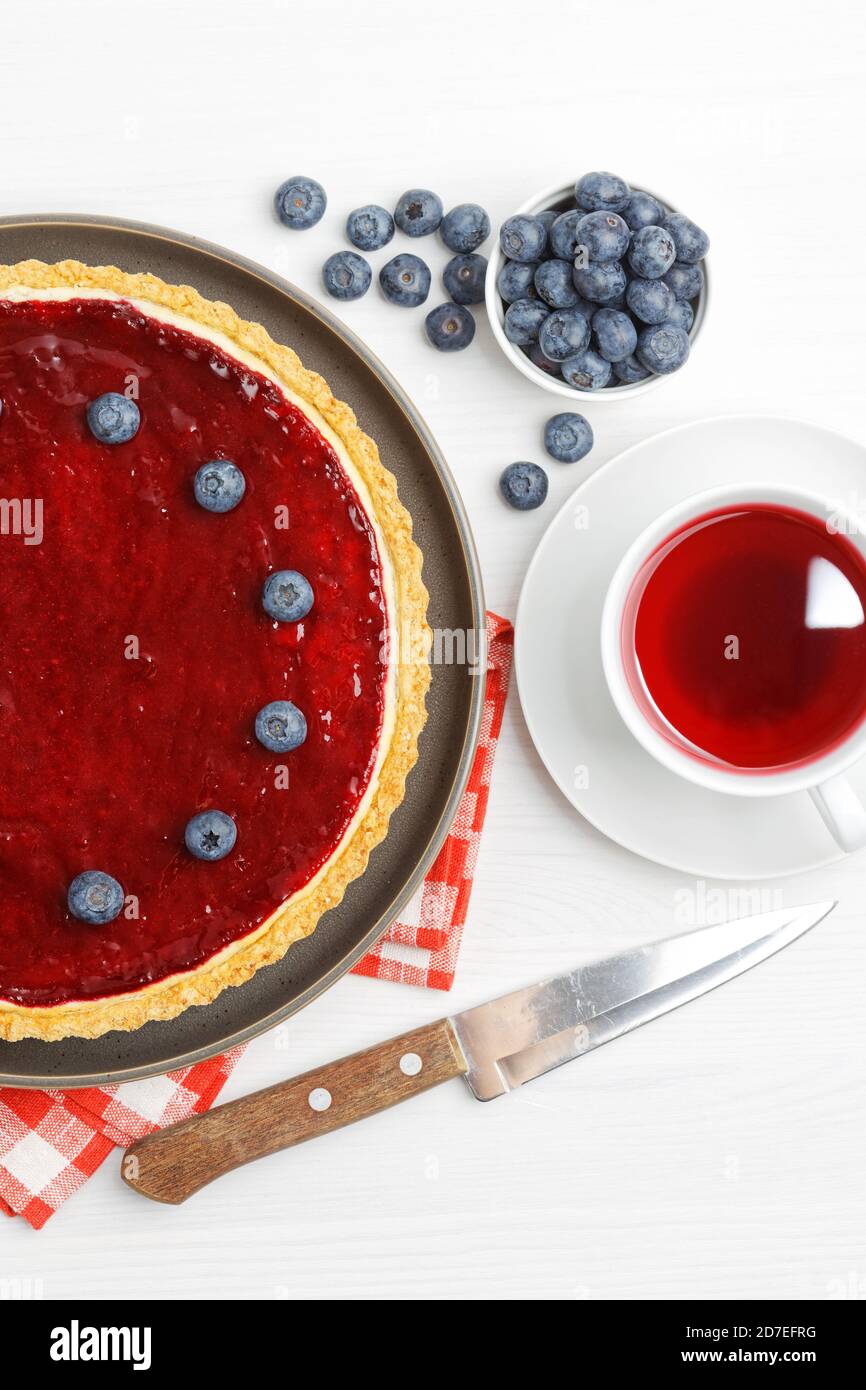 Cheesecake maison avec gelée de baies et une tasse d'hibiscus de thé rouge sur une table en bois blanc. Vue de dessus. Banque D'Images
