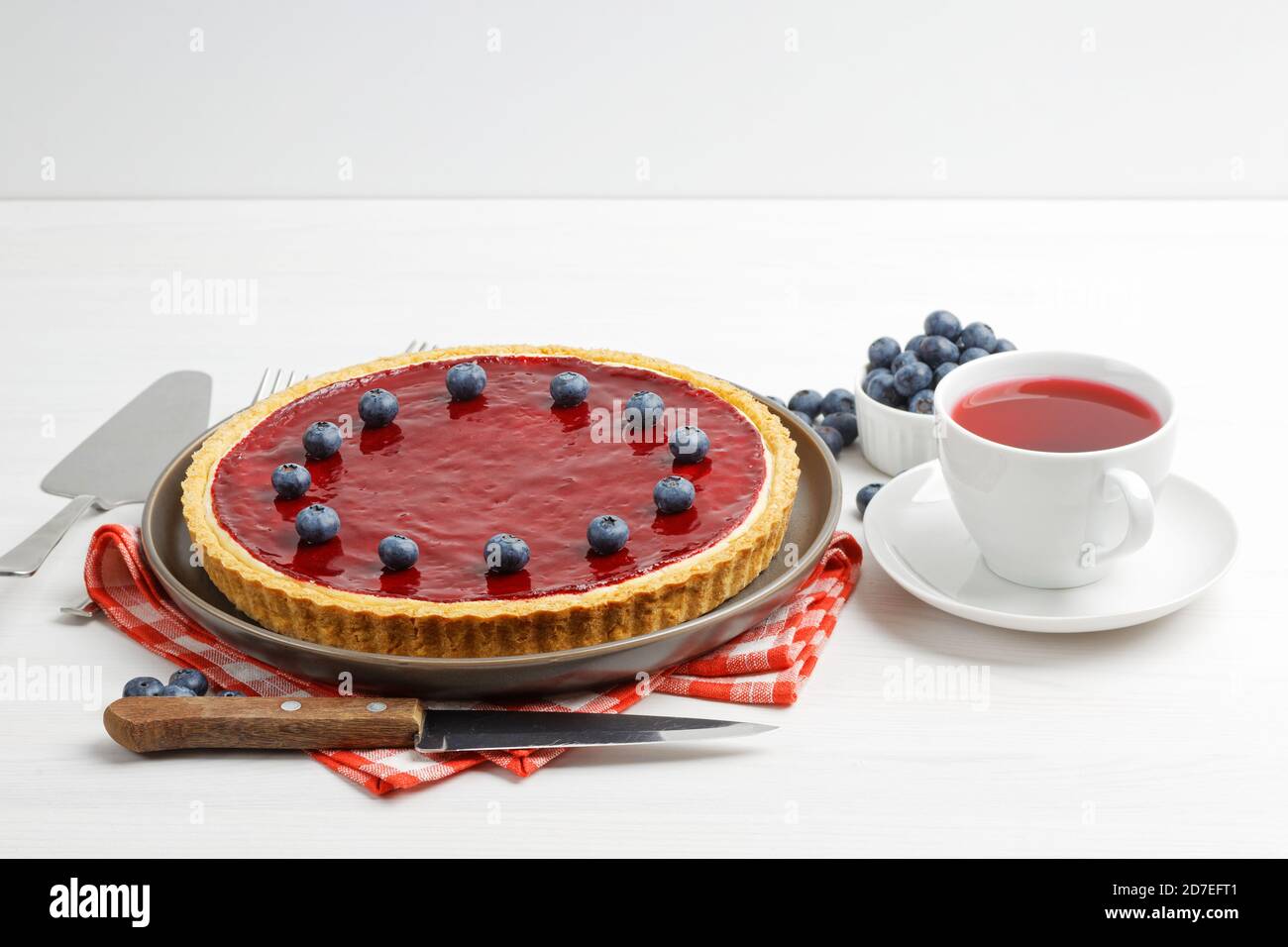 Cheesecake maison avec gelée de baies et une tasse d'hibiscus de thé rouge sur une table en bois blanc. Banque D'Images