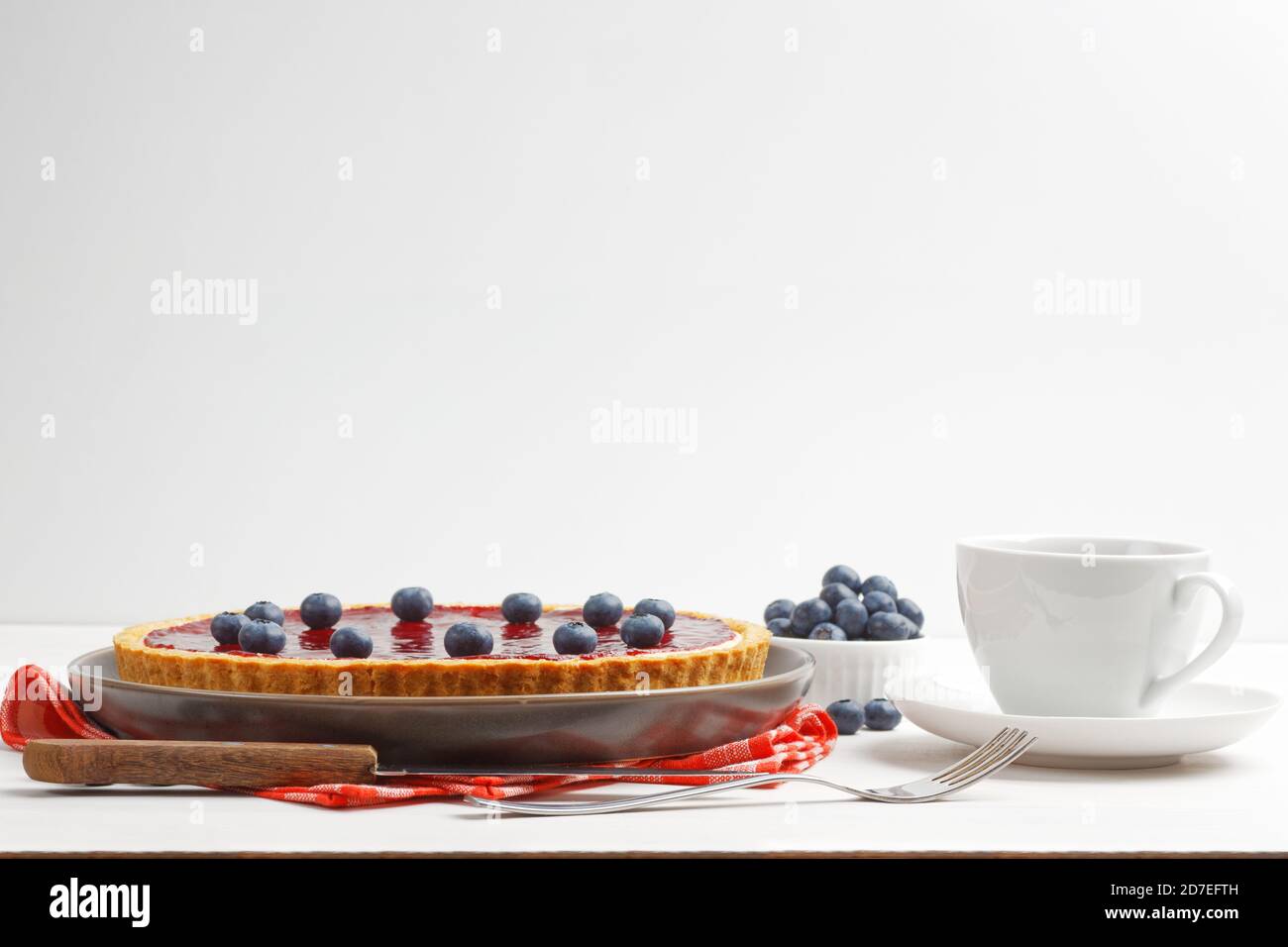 Cheesecake maison avec gelée de baies et une tasse de thé ou de café sur une table en bois blanc. Vue avant. Copier l'espace. Banque D'Images