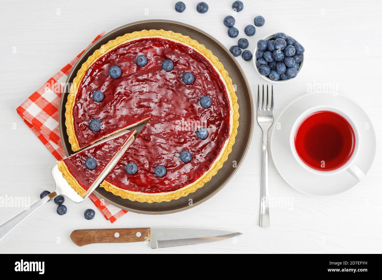 Cheesecake maison avec gelée de baies et une tasse d'hibiscus de thé rouge sur une table en bois blanc. Vue de dessus. Banque D'Images
